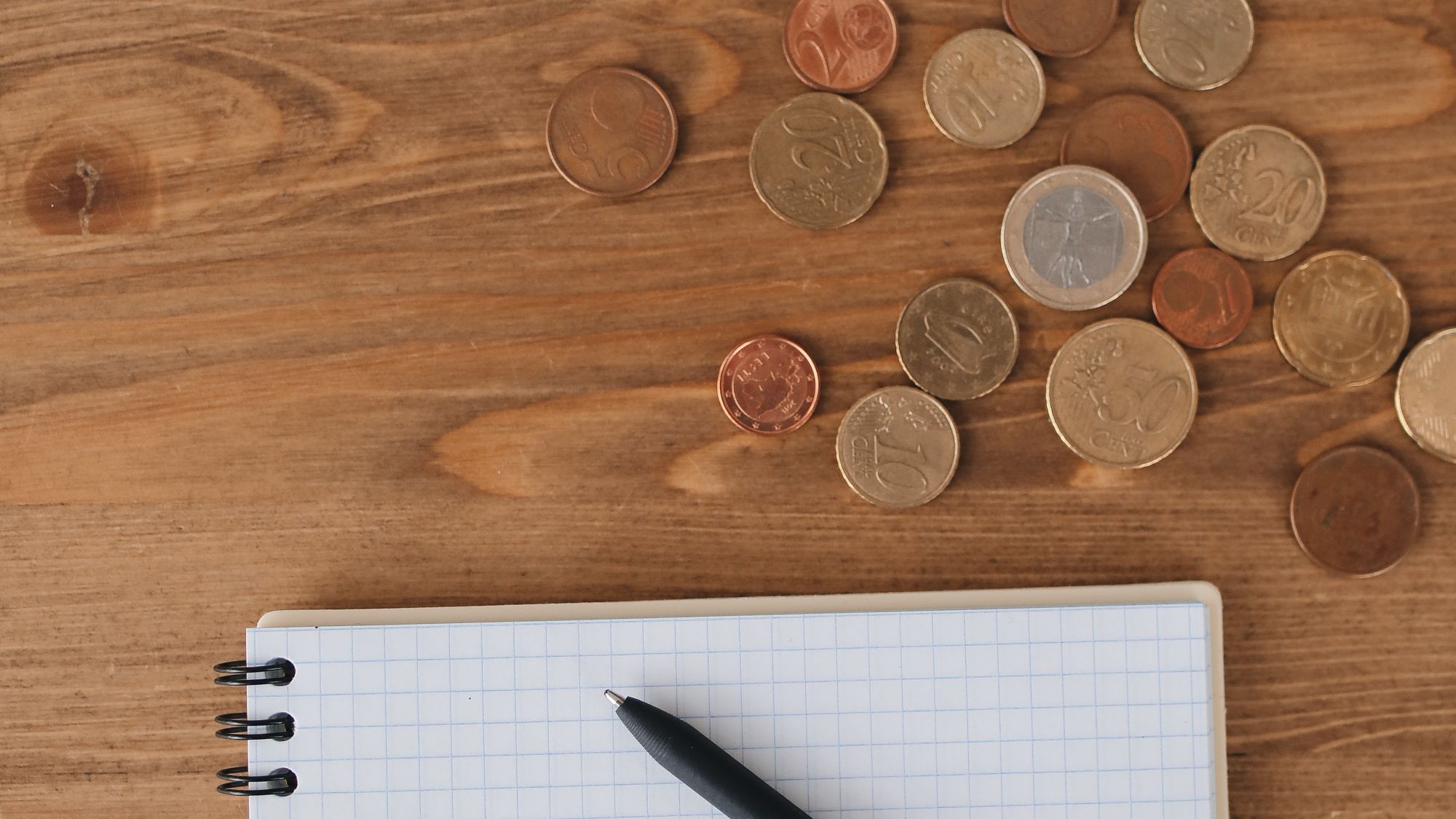 Coins scattered on a desk beside a notebook and pen for budgeting