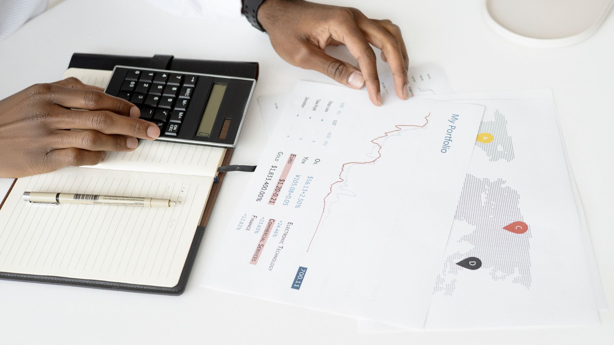 Hands using a calculator next to printed charts while analyzing data